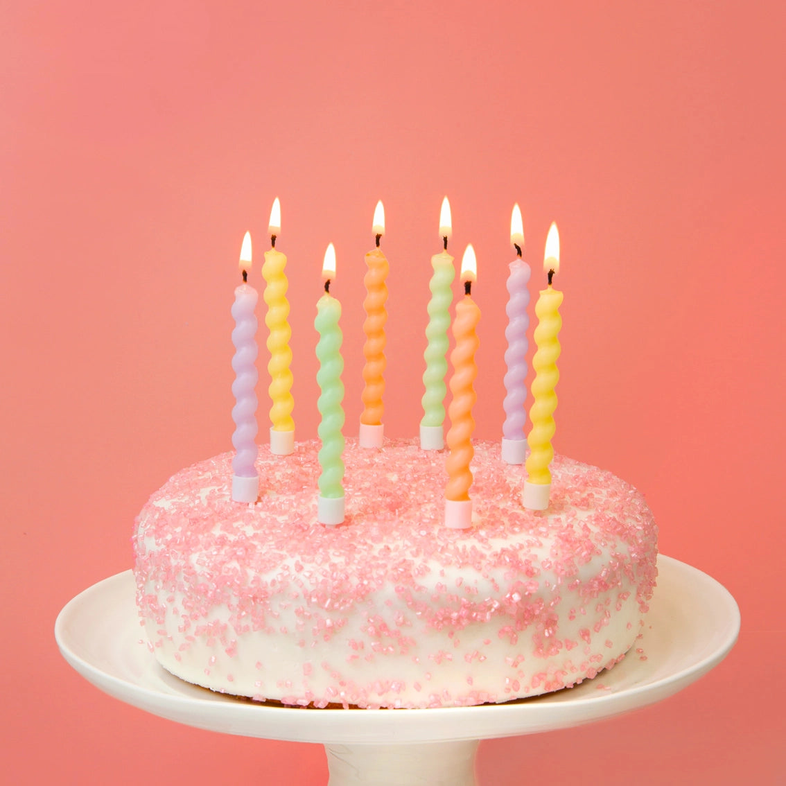 Pastel spiral birthday candles on a pink frosted cake with sugar sprinkles.