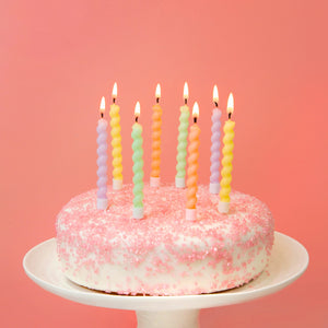Pastel spiral birthday candles on a pink frosted cake with sugar sprinkles.
