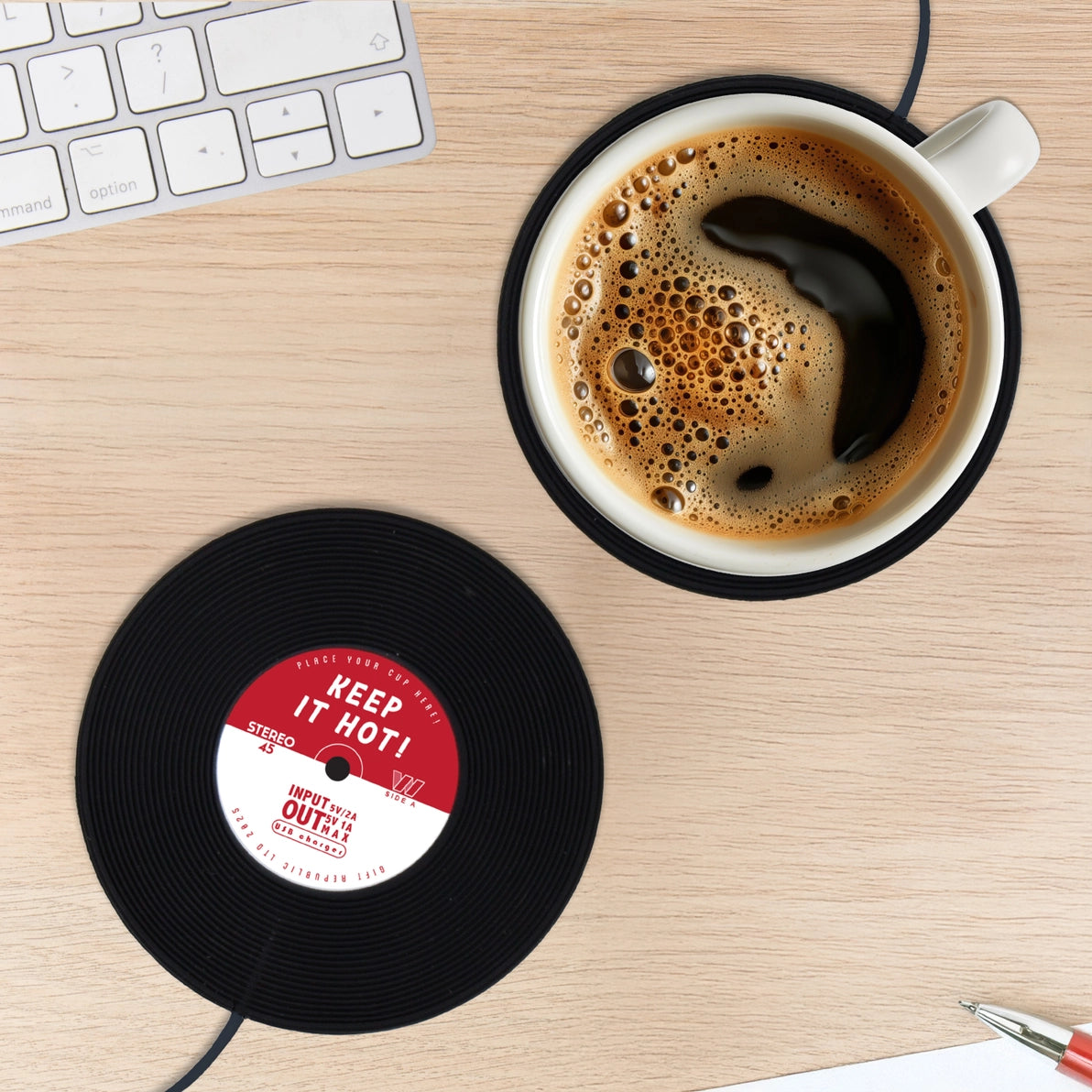 USB-powered vinyl record mug warmer on a wooden desk with a hot coffee mug placed on top, next to a computer keyboard – perfect desktop accessory for keeping drinks warm.