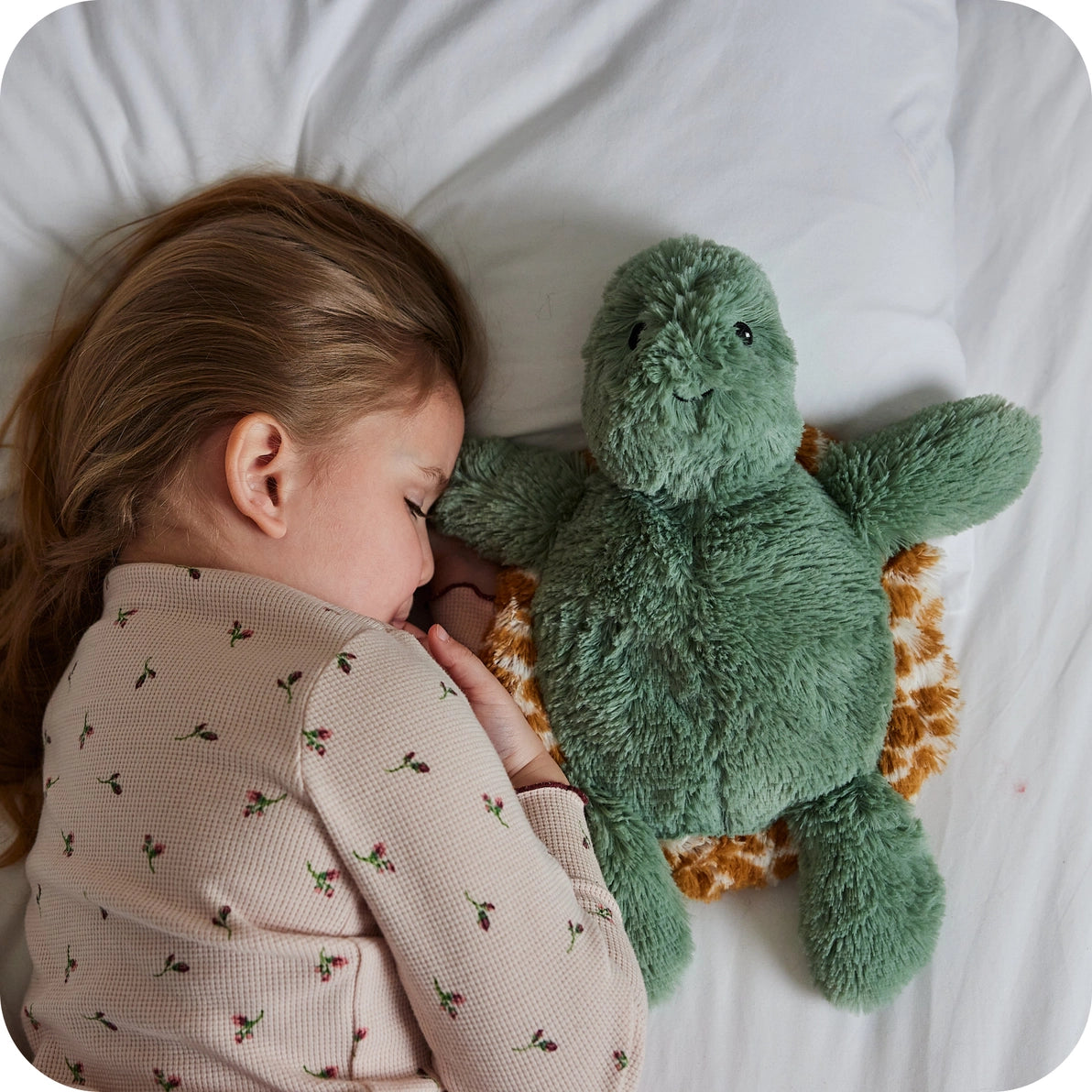 Child cuddling Warmies Baby Turtle soft toy in bed for soothing comfort.