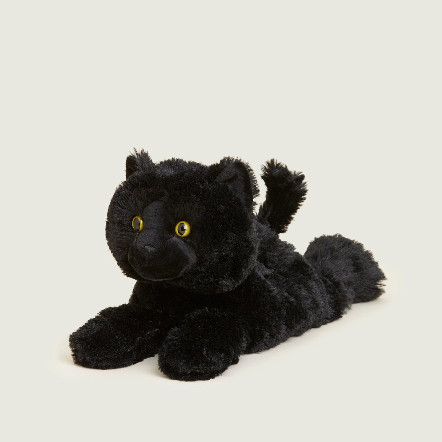 Warmies Black Cat microwavable plush toy with soft black fur and bright yellow eyes, lying down on a neutral background.