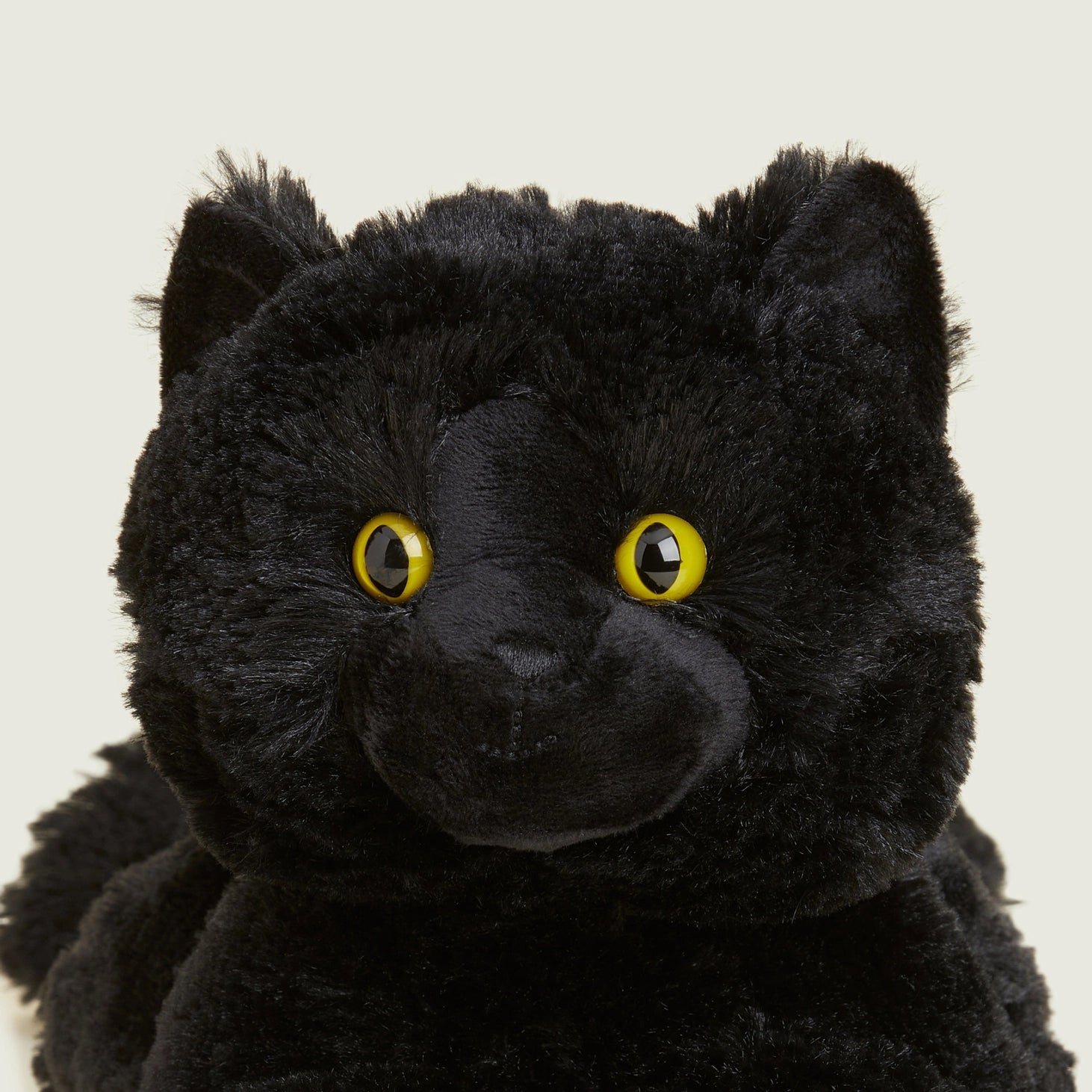 Close-up of Warmies Black Cat face showing detailed stitching, bright yellow eyes, and velvety black plush fur.