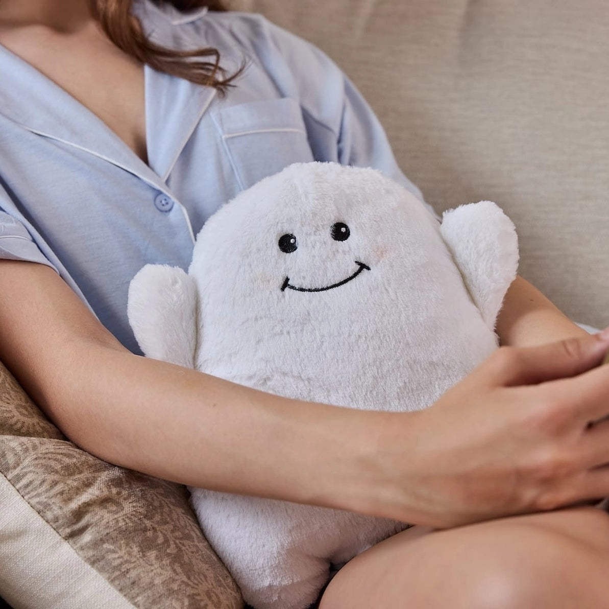 Woman holding Warmies Ghost plush while sitting on sofa, showing size and comfort.