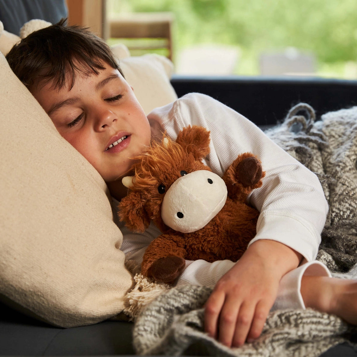 Child cuddling Warmies Junior Highland Cow heatable lavender plush.