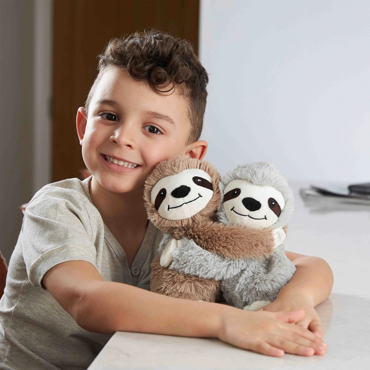 Child hugging Warmies Warm Hugs Sloths soft plush lavender-scented toys.