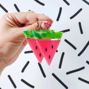 Pair of bold watermelon earrings held in hand, showing vibrant recycled acrylic design with bright green rind, neon pink flesh and painted seed detail.