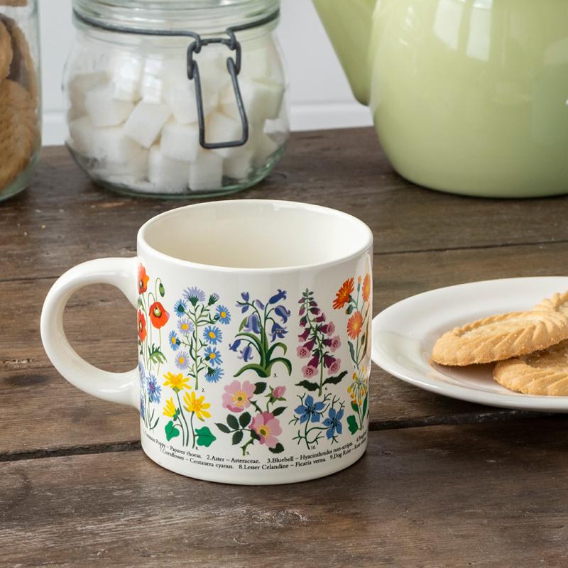 Wild Flowers ceramic mug on a rustic table beside a plate of biscuits, sugar jar, and teapot.