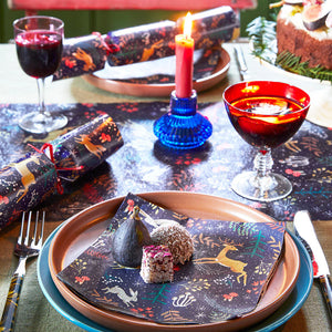 Festive dinner table with reindeer cracker, red cocktail, and Woodland Flora napkin placed on a plate for Christmas dining.
