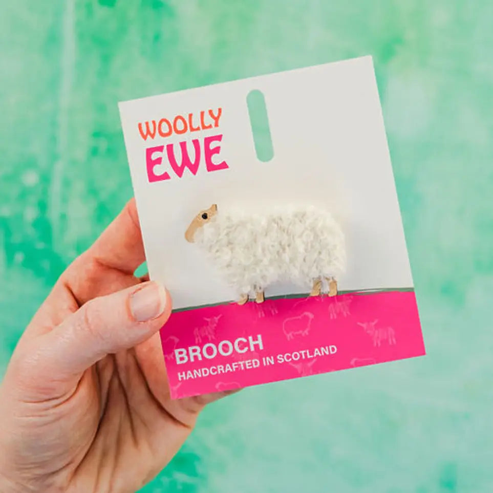 Handcrafted Woolly Ewe brooch on branded card with pink label, featuring fluffy white wool and wooden sheep design, made in Scotland.