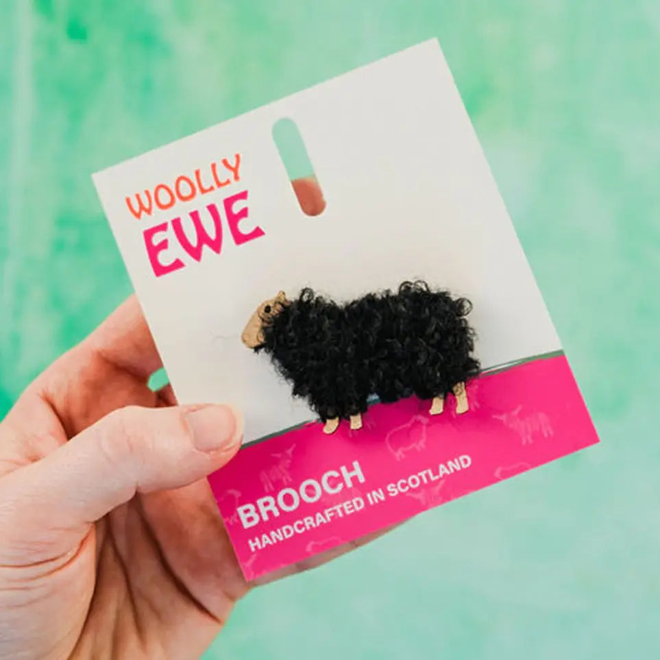 Handcrafted black Woolly Ewe brooch named Iona on branded card, featuring dark wool and wooden sheep detailing, made in Scotland.