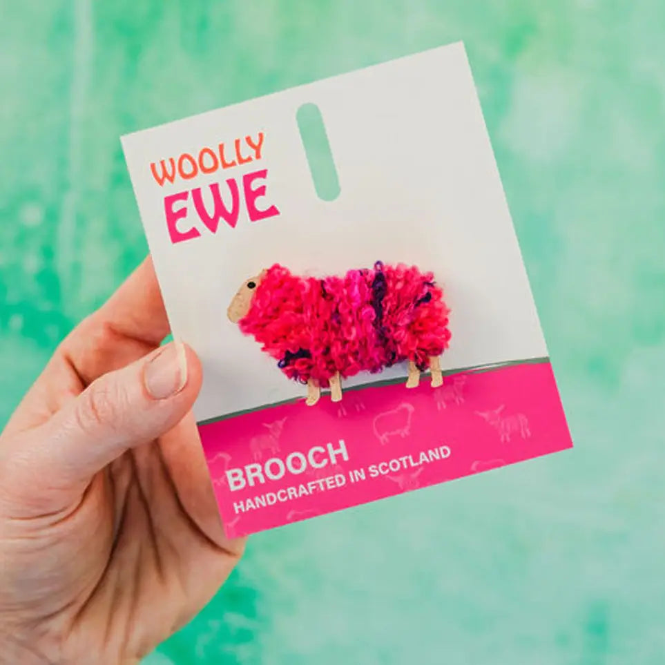 Hand holding Woolly Ewe Maisie brooch on backing card with pink and purple fluffy wool