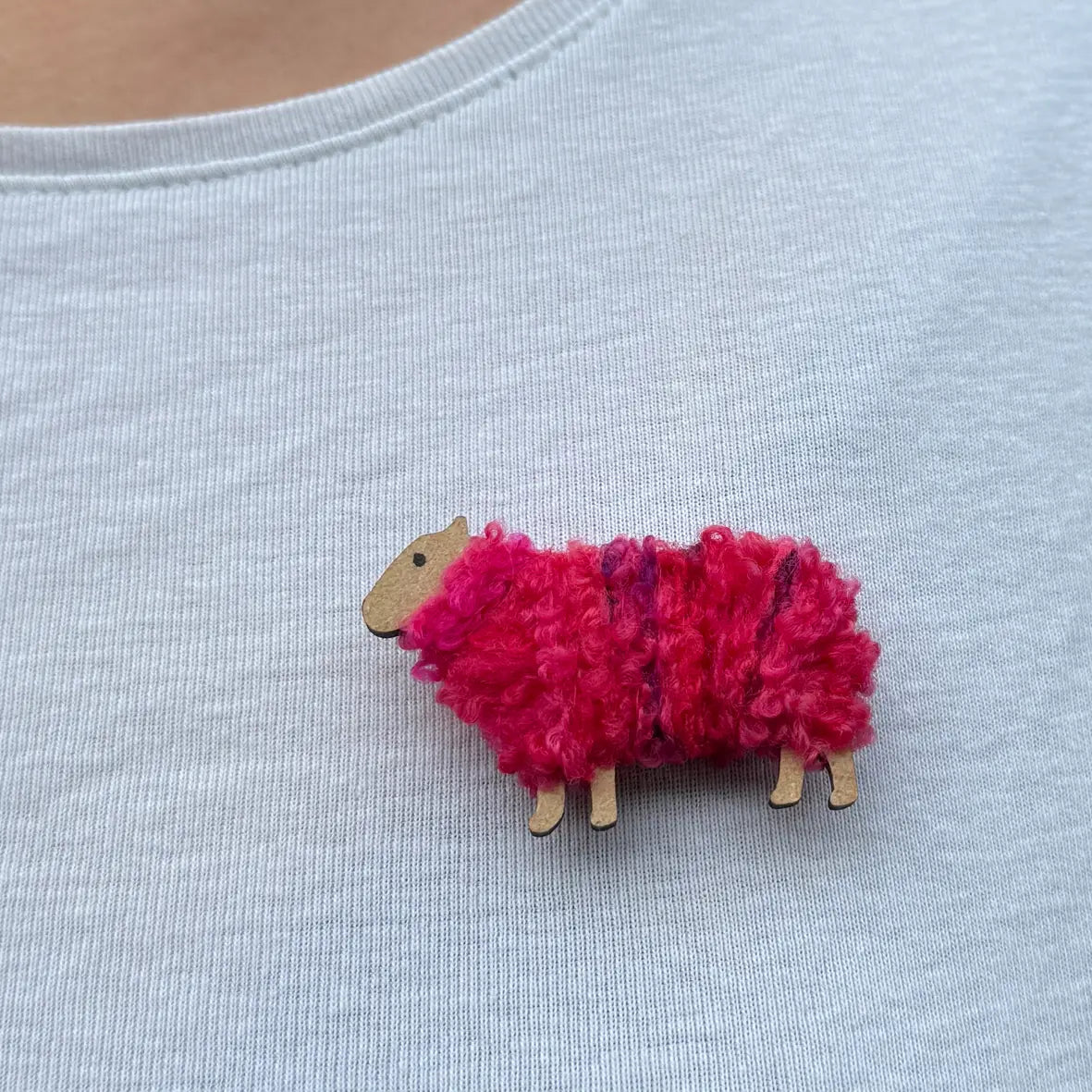 Pink Maisie Woolly Ewe brooch pinned to light blue top, handcrafted from wool and wood.