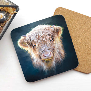 Close-up of the Little Highlander Highland Cow Coaster featuring a fluffy young Highland cow on a dark blue background, with a cork backing partially visible.