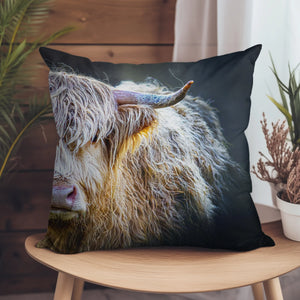 A luxurious Peekaboo Highland Cow suede cushion on a wooden chair, showcasing its rustic and cosy design.