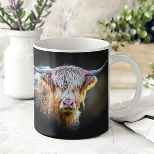 A ceramic mug featuring the “Shadow Gaze” Highland cow design by Gary Cox, placed on a white surface with a blurred background of plants and a white vase.