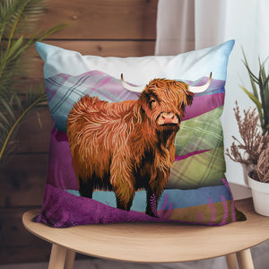 A vibrant Tartan Highland Cow suede cushion on a wooden chair, featuring a striking Highland cow against a rich tartan landscape.