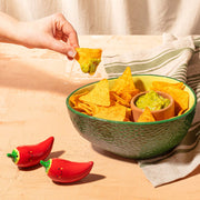 Green avocado-shaped chip and dip bowl filled with tortilla chips and guacamole with hand dipping a chip