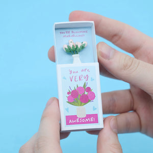 Opened matchbox revealing a tiny vase of pink roses with a heartfelt message inside.