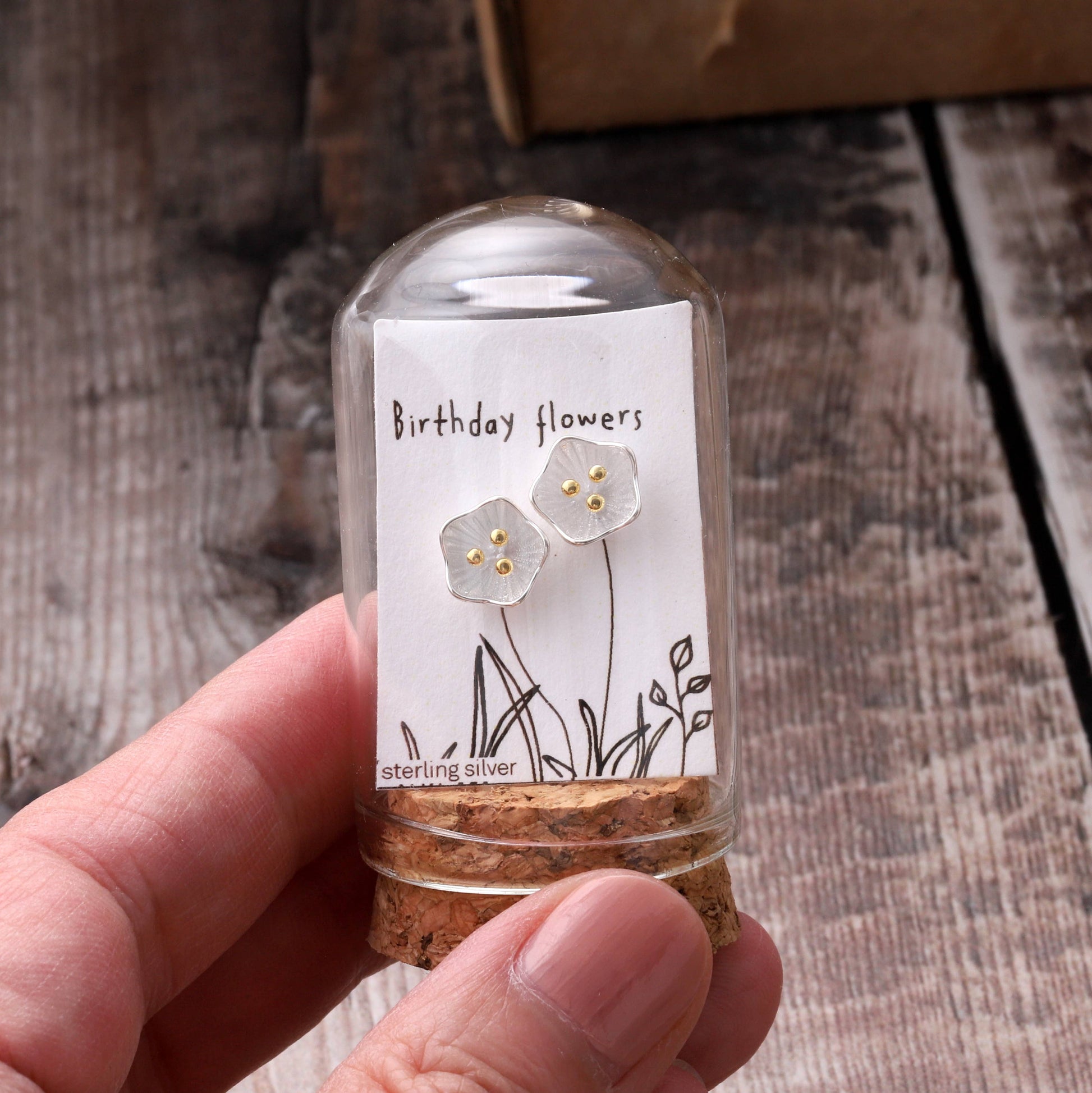 Sterling silver flower stud earrings on birthday message card inside glass terrarium held in hand