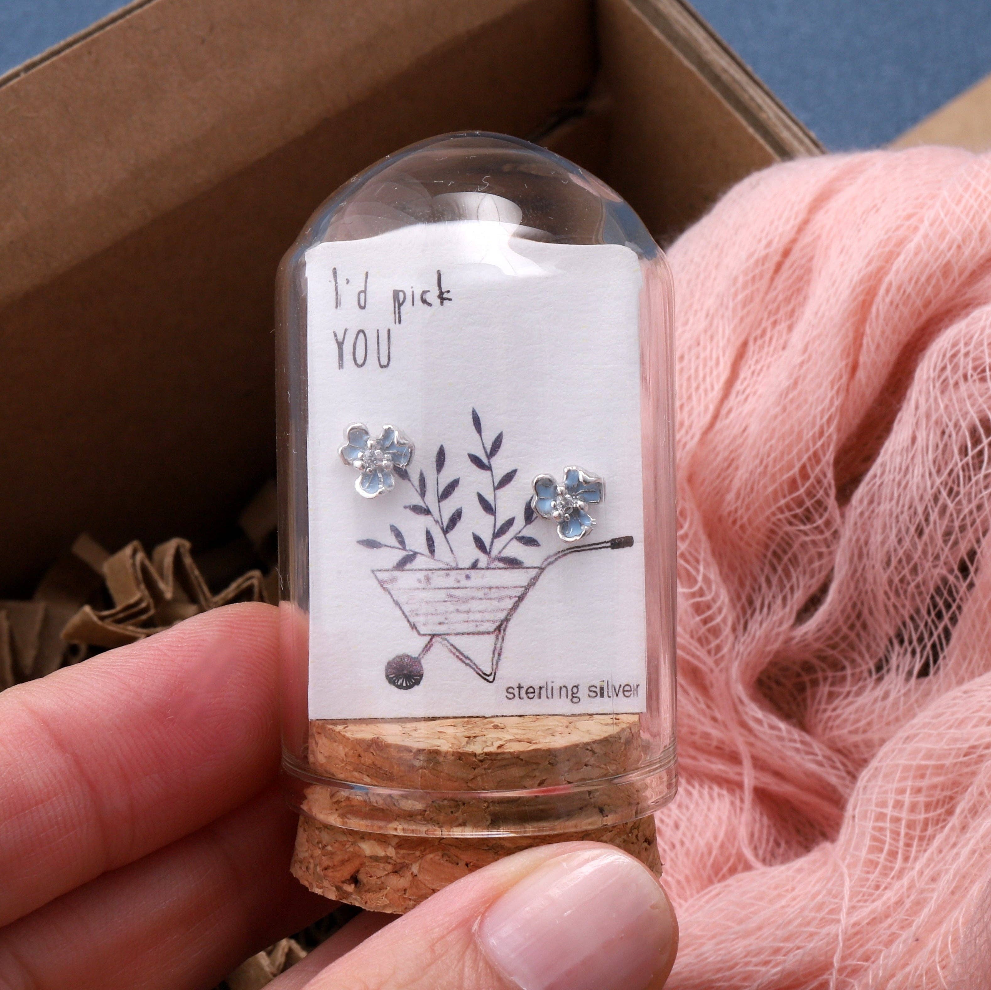 Blue three-petal flower earrings on message card inside glass terrarium held in hand