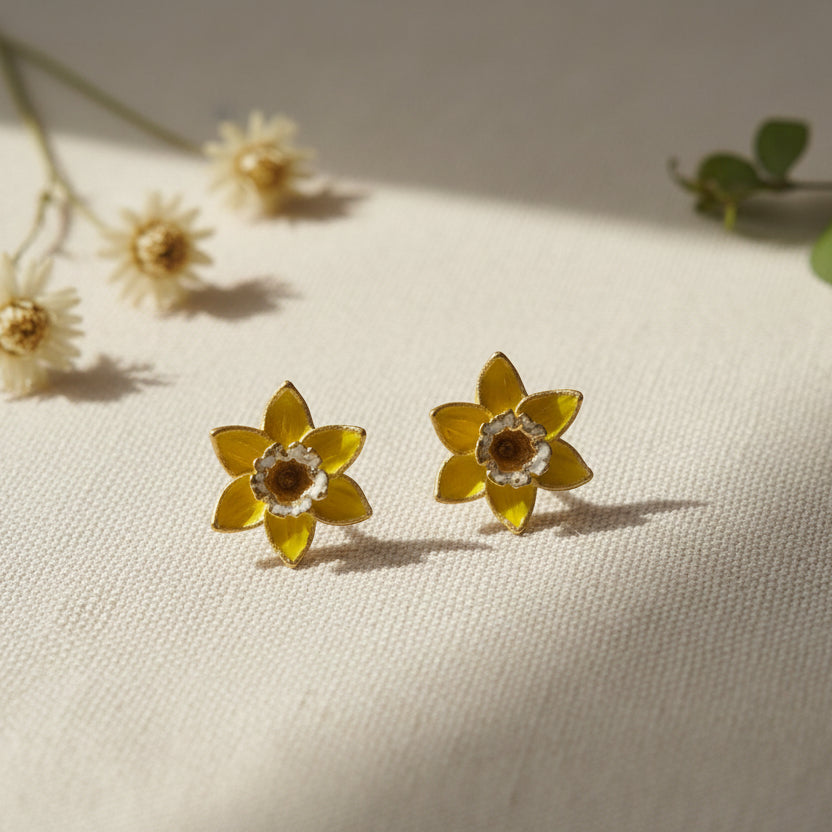 Yellow daffodil stud earrings with gold detailing on natural linen fabric with dried flowers