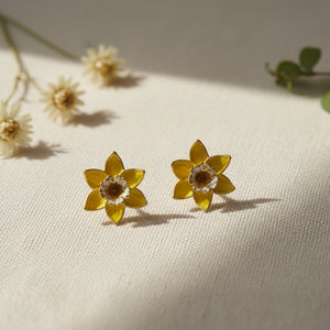 Yellow daffodil stud earrings with gold detailing on natural linen fabric with dried flowers