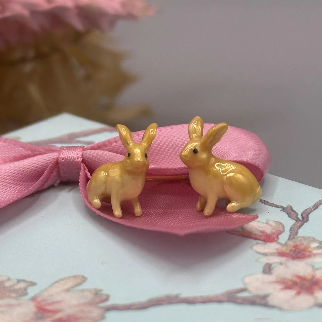 Pair of Bill Skinner enamel rabbit stud earrings in yellow displayed on a pastel gift box with pink ribbon.