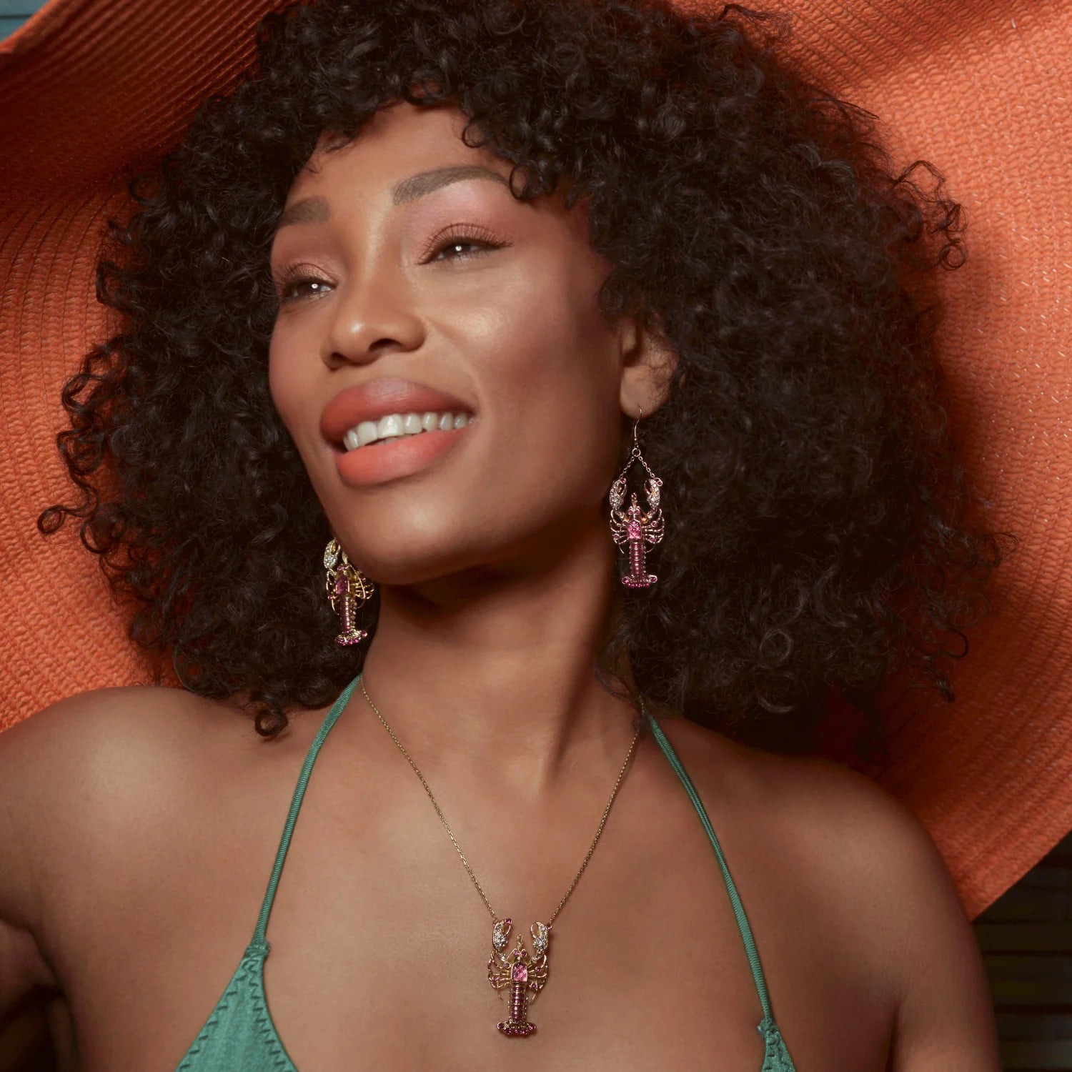 Model wearing Bill Skinner lobster drop earrings and matching necklace with wide orange hat.