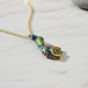 Blue and green enamel peacock pendant necklace with gold chain displayed on light marble surface