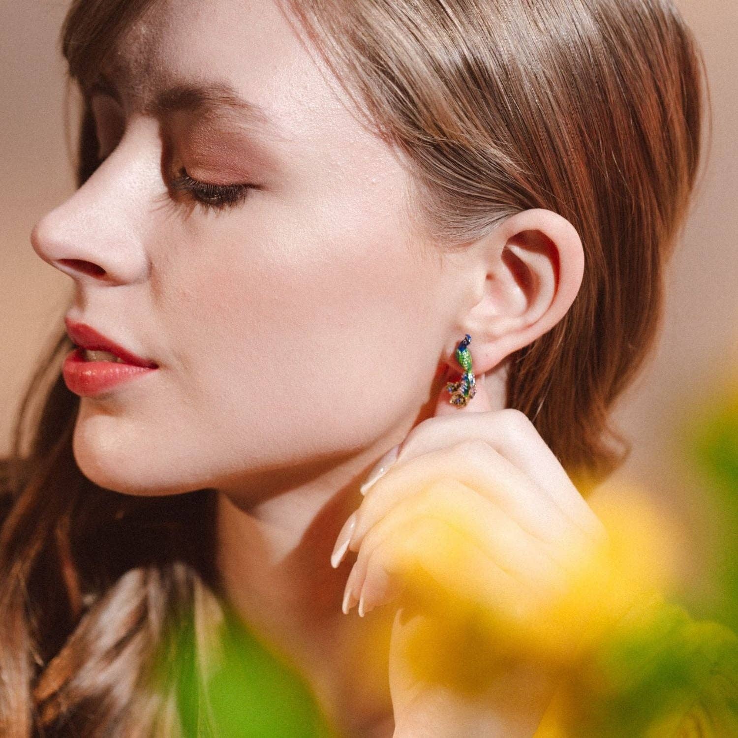 Hand holding peacock stud earring showing scale.