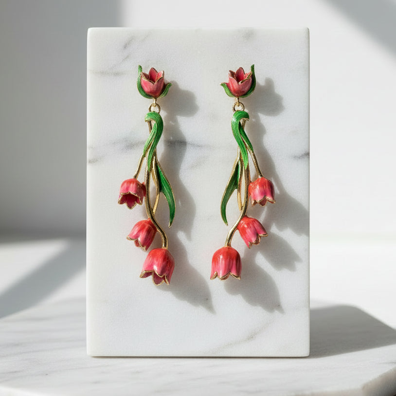 Red tulip drop earrings with gold accents and green enamel leaves displayed on cream marble tile
