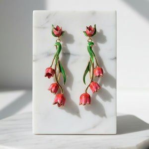 Red tulip drop earrings with gold accents and green enamel leaves displayed on cream marble tile