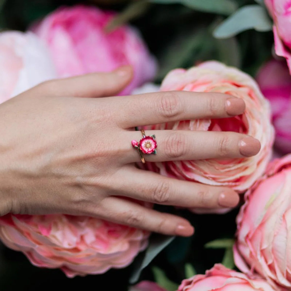 Model wearing Bill Skinner Wild Flower Open Ring surrounded by pink peonies, showing delicate floral design and gold finish.