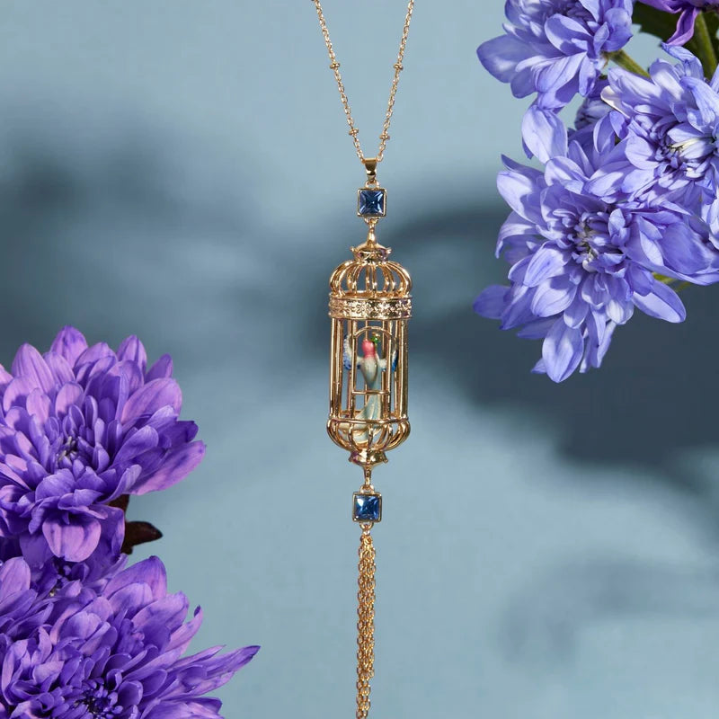 Bird Cage Pendant displayed among flowers, highlighting its intricate enamel detailing.