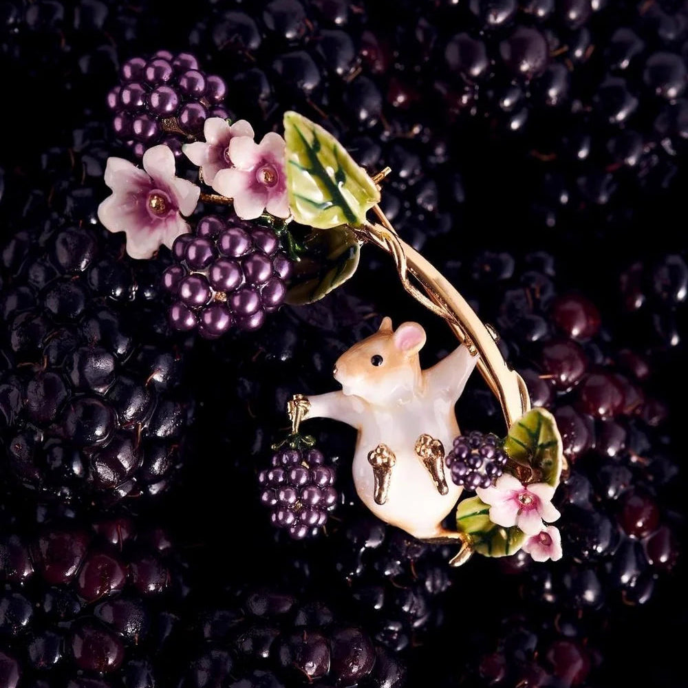 Blackberry & Mouse Brooch resting among fresh blackberries, showing hand-painted enamel detail and gold finish.