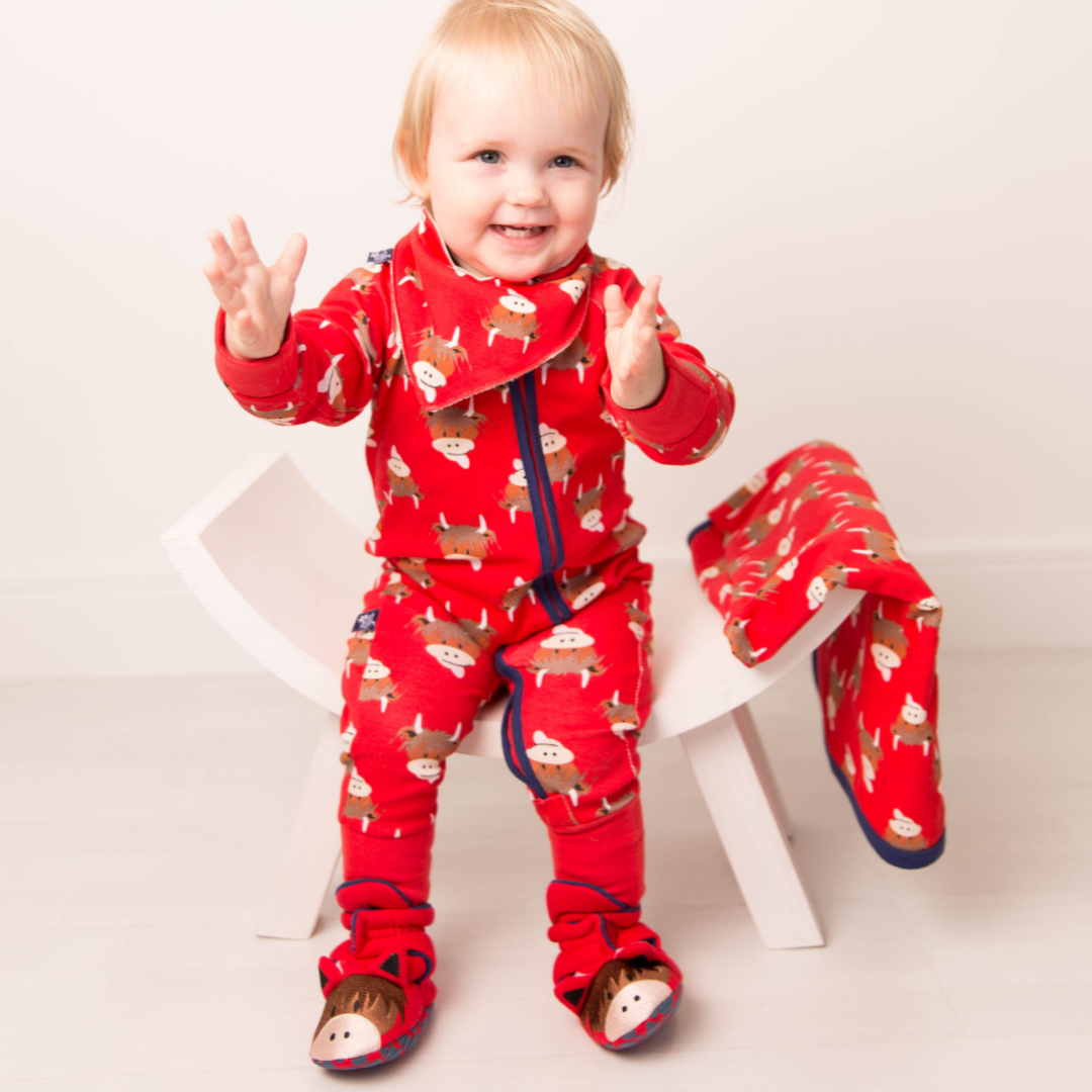 Smiling baby standing in red highland cow zip-up romper