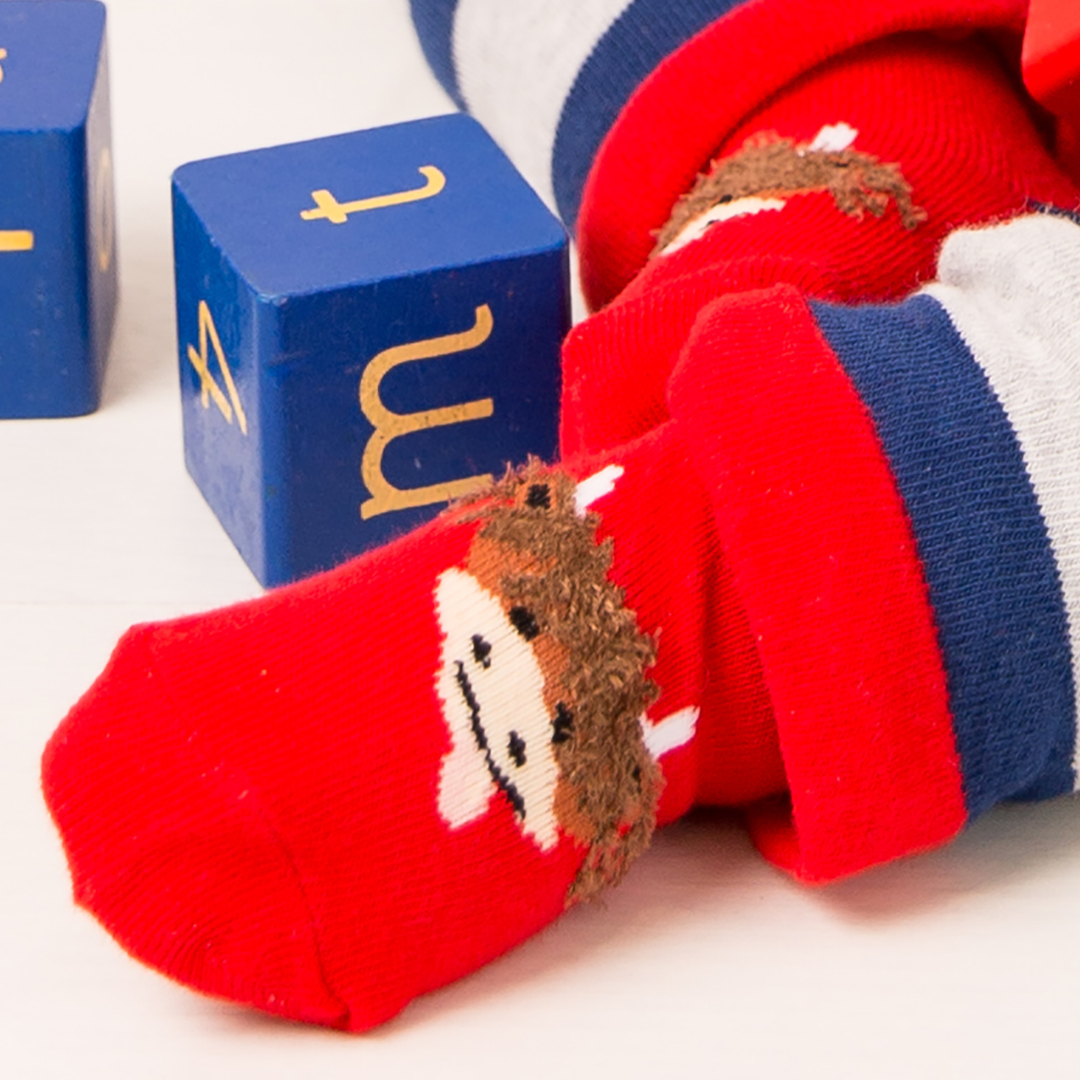 Baby wearing red highland cow socks next to blue blocks