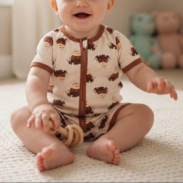 Baby wearing cream highland cow romper with brown zip