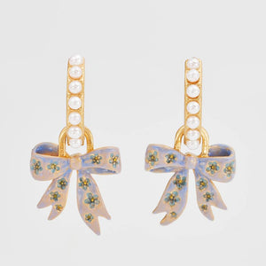 Straight-on view of the earrings showing pearl-set hoops with dangling hand-painted bow charms.