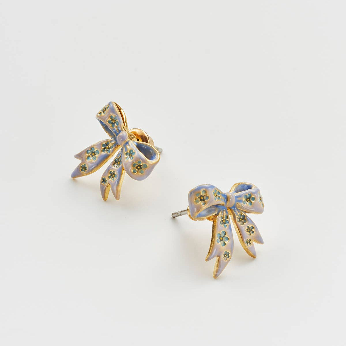 Gold bow stud earrings with enamel detail shown at an angle