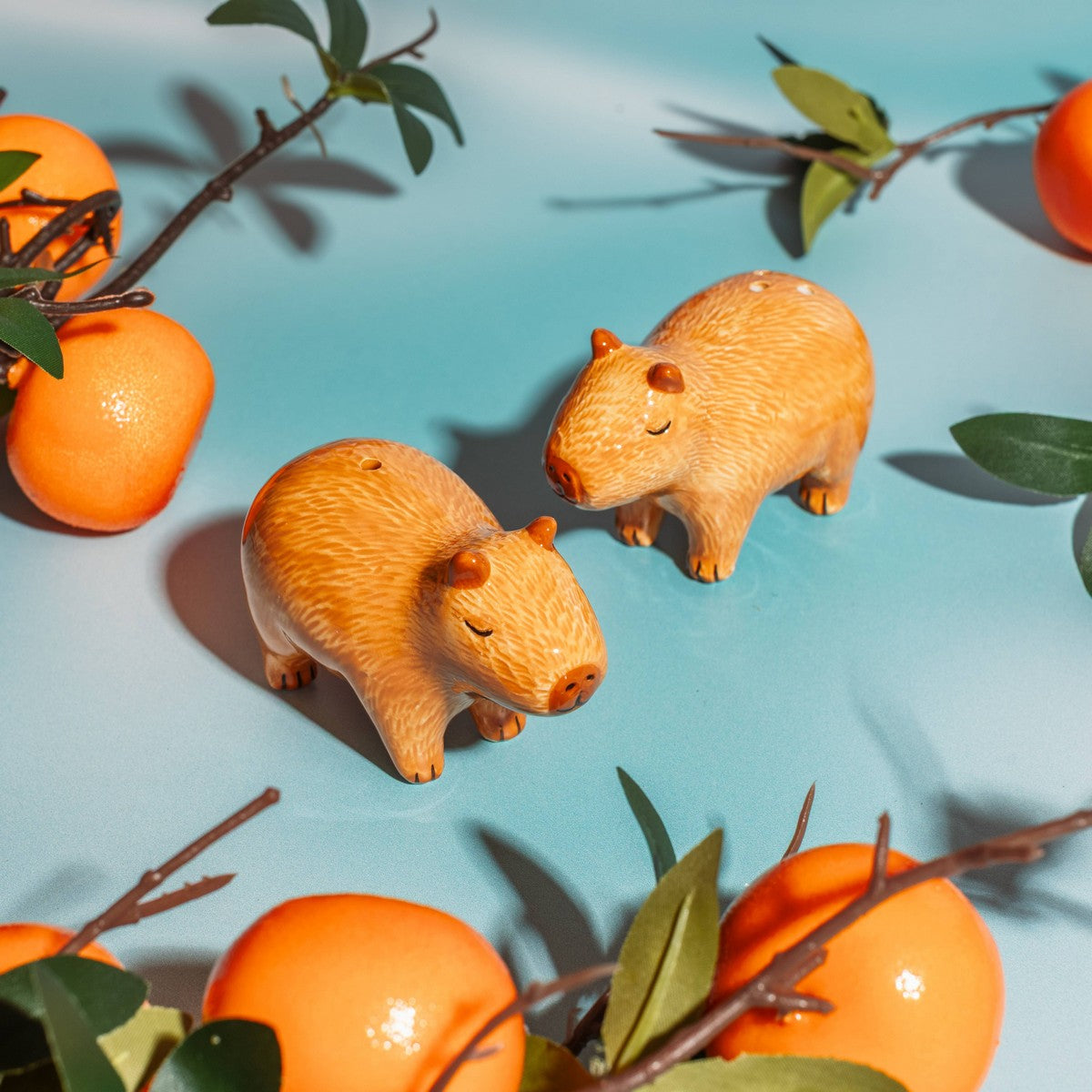 Capybara salt and pepper shakers on teal background with oranges