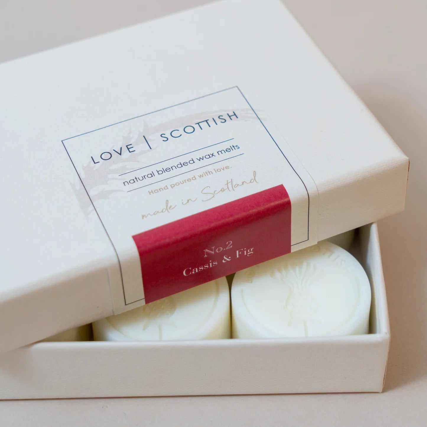 Box of Cassis & Fig wax melts in cream packaging with Scottish branding, partially opened to show round soy wax melts inside.
