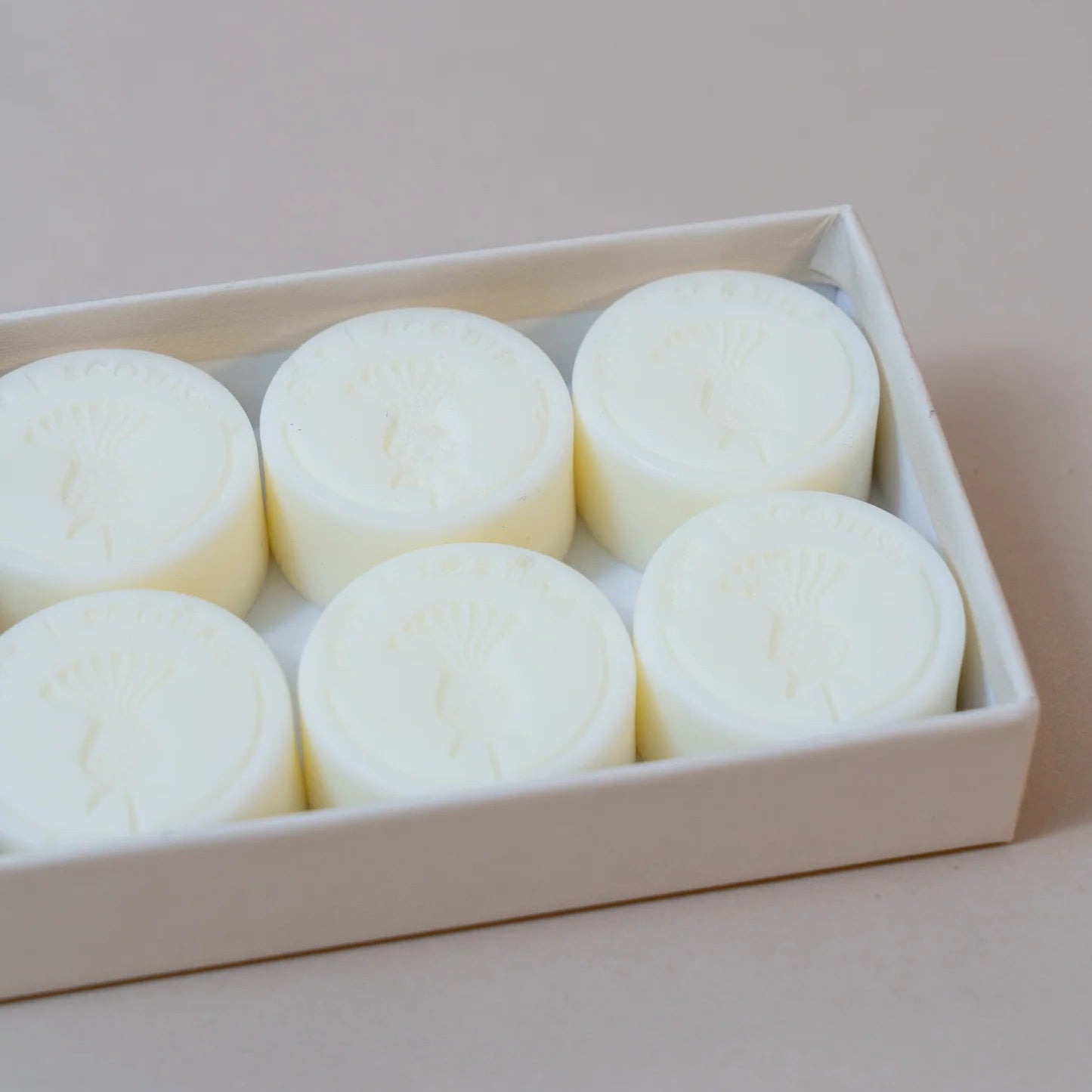 Close-up of Cassis & Fig wax melts in an open cream box, showing embossed thistle design on each melt.