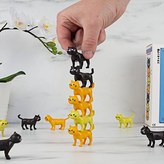Hand stacking black and yellow cat pieces into a tall tower for Catastrophe game.