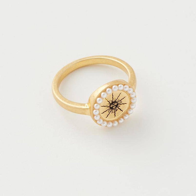 Celestial Ring close-up showing gold sun charm with pearl border on grey background