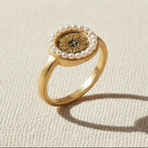 Celestial Ring gold-plated with pearl-encircled sun charm on cream fabric background