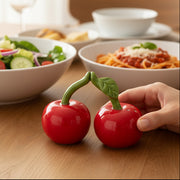 Cherry salt and pepper shakers on wooden table with pasta dish