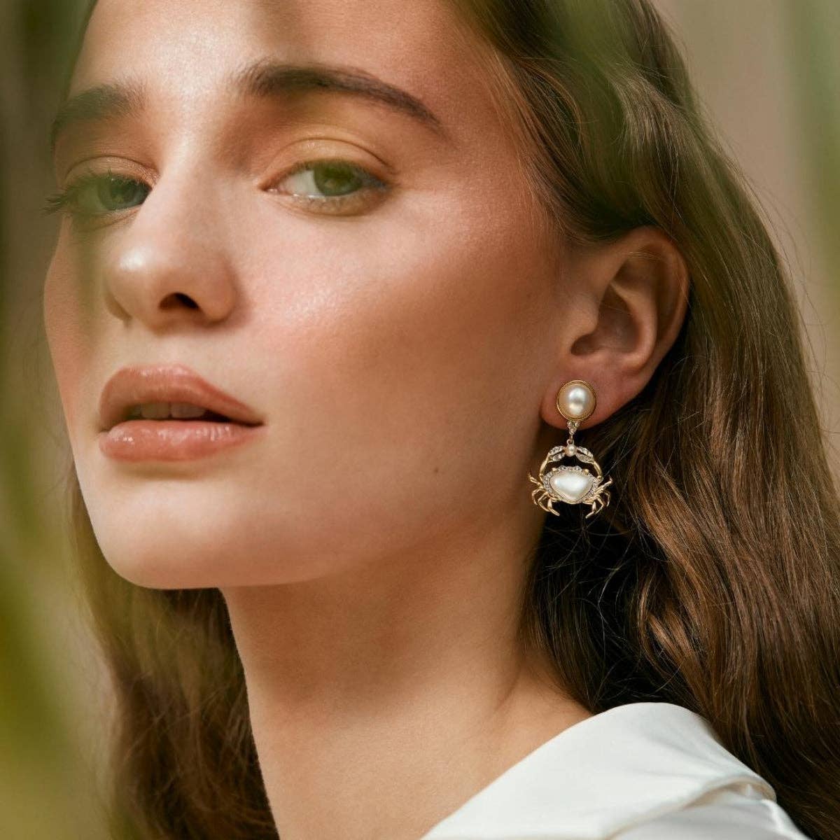 Model wearing gold crab drop earrings with pearlised resin body.