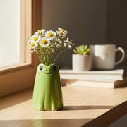 Adorable green ceramic frog mini vase holding white daisies and baby's breath flowers on a wooden surface