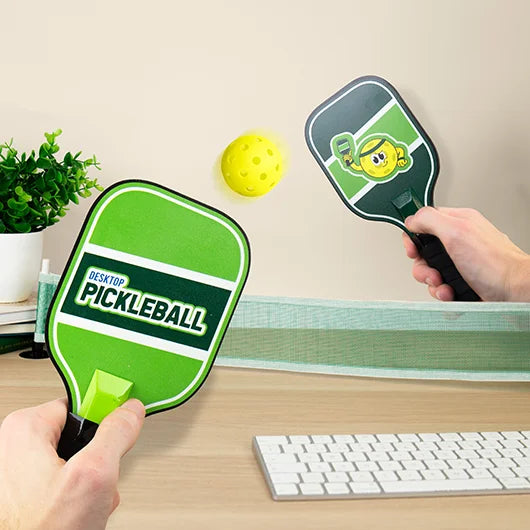 Two people playing desktop pickleball with mini net on a desk